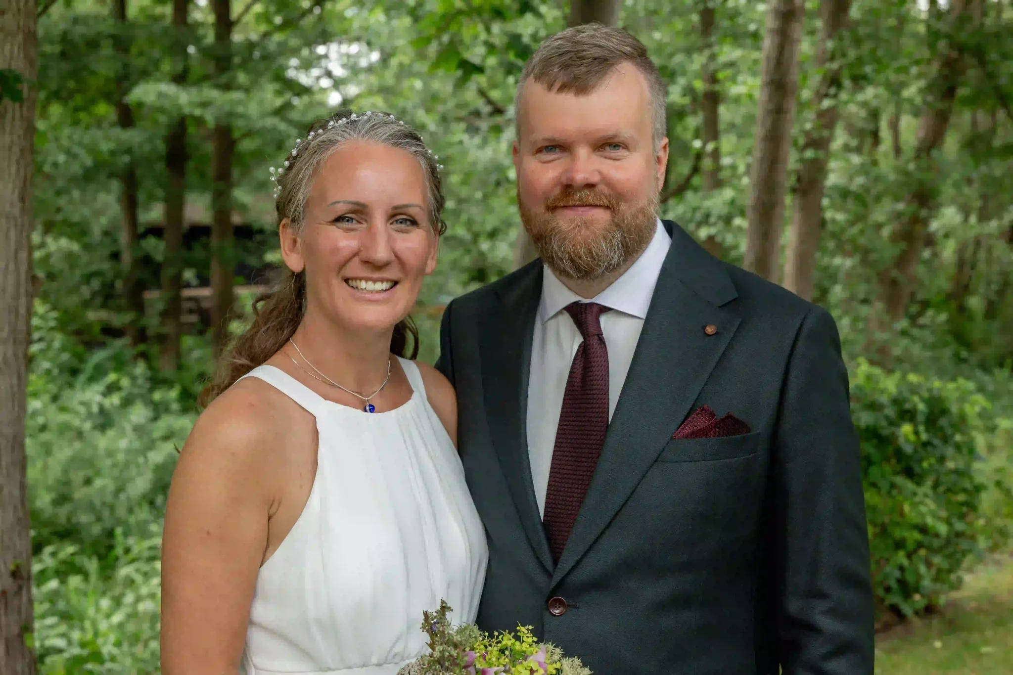 Festfotograferne har her fotograferet et brudepar, der står sammen og smiler i de grønne omgivelser.
