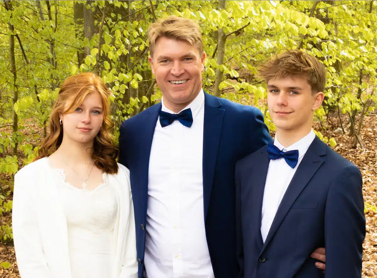 Festfotograferne har her fotograferet til en konfirmation af et tvillingepar. På dette billede ses en far med sin tvillingedatter ved den ene side og sin tvillingesøn ved den anden side. Skoven ses i baggrunden