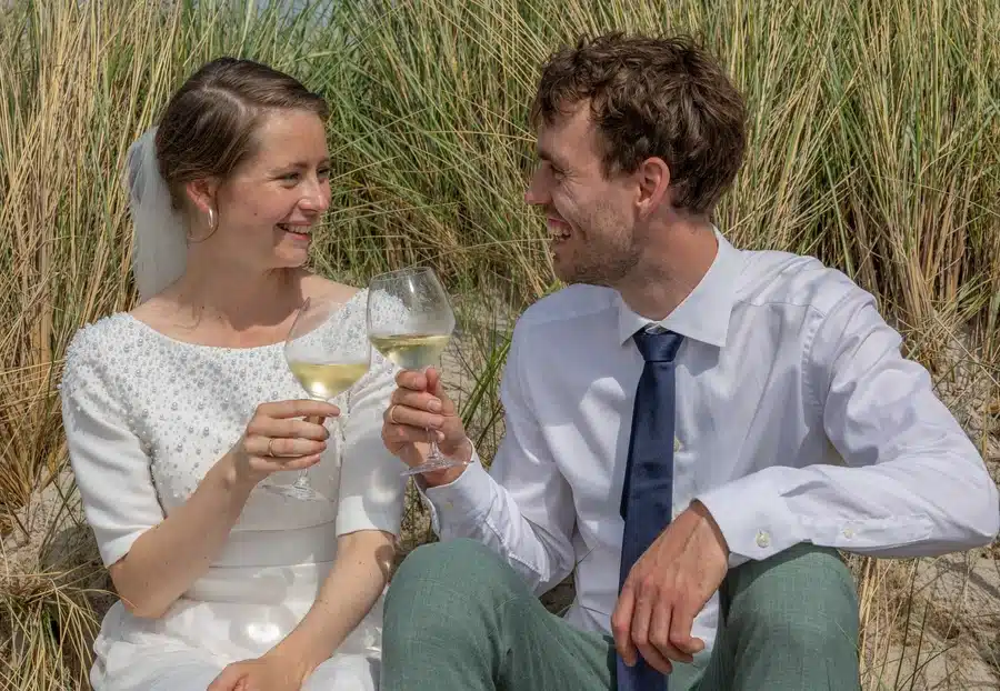 Priser 3 Festfotograferne har her fotograferet brudeparret, der sidder i klitterne og skåler med et glas vin på deres bryllupsdag.