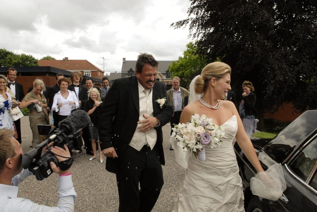 Festfotograferne har her filmet og fotograferet ved et bryllup. Brudeparret ses på billedet på vej fra kirken hen mod deres bil. Gæsterne står i baggrunden og kaster med ris