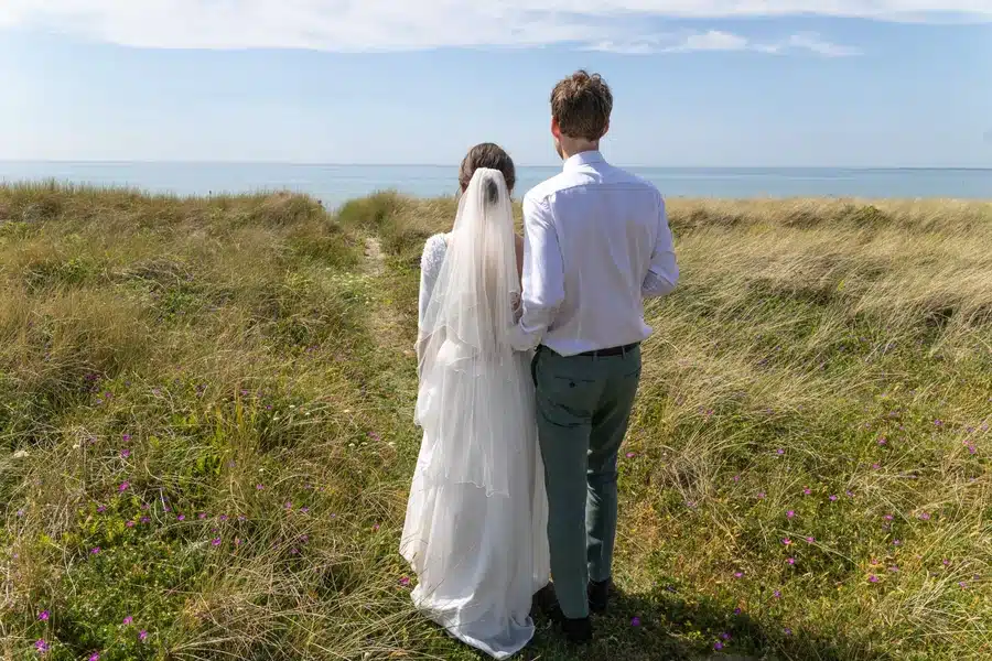 Bryllup 13 Festfotograferne har her fotograferet et brudepar, der står sammen i klitterne med udsigt over havet på deres bryllupsdag.