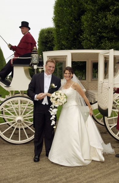 Festfotograferne har her fotograferet et Brudepar opstillet foran karet. Kusken ses sidde oppe på karetten i baggrunden. Bruden holder slæber på sin kjole i den ene hånd og en brudebuket i hvide nuancer i den anden. Gommen, der er i sort jakkesæt og hvid skjorte står ved hendes side
