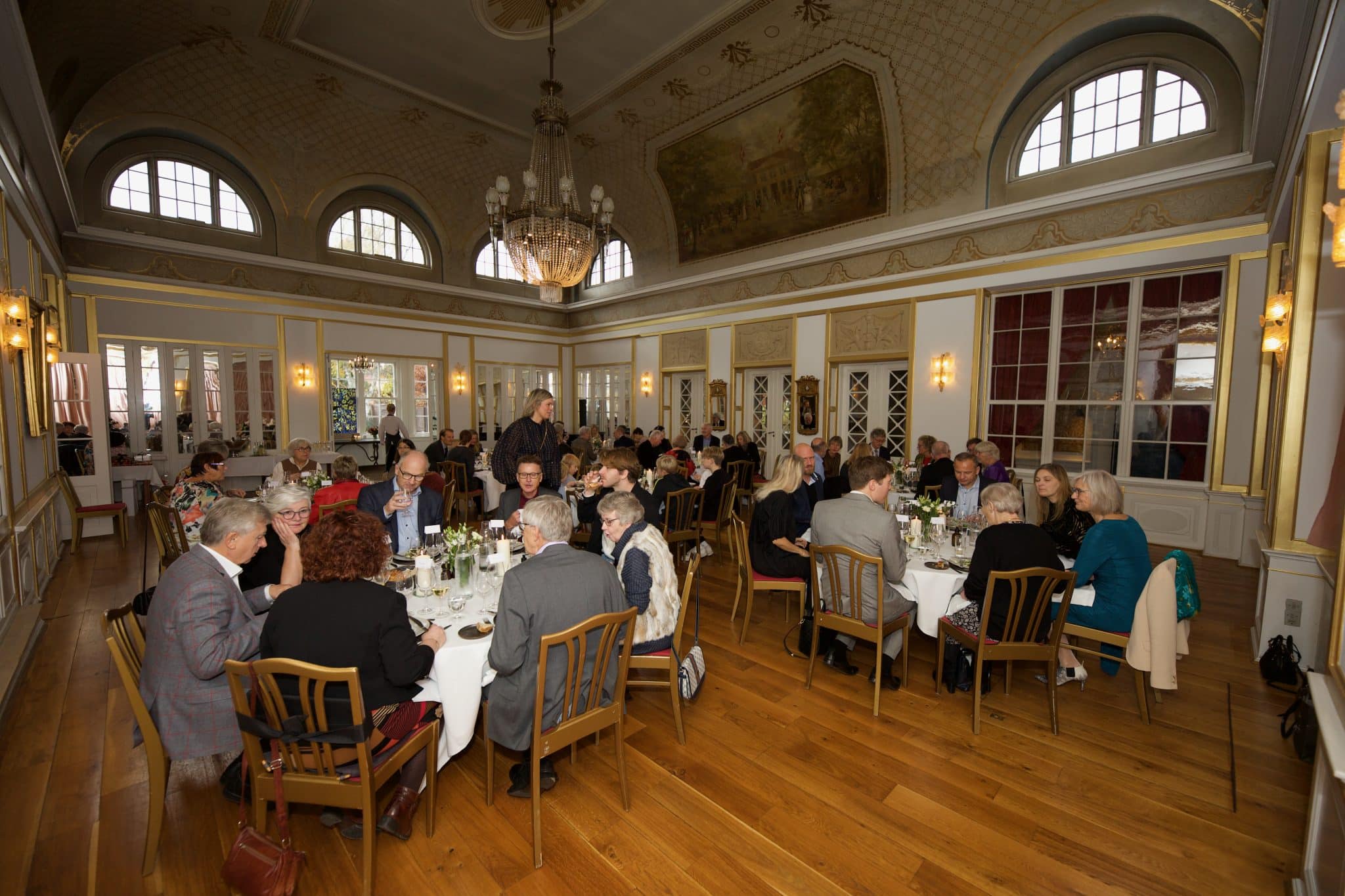 Festfotograferne har her fotograferet til en fødselsdag. På billedet ses gæsterne sidde i en stor sal ved runde borde.