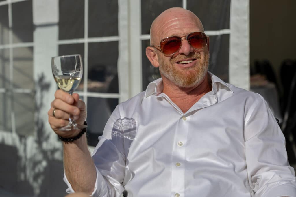 Skaldet mand med solbriller sidder med vinglas i hånden og nyder solen