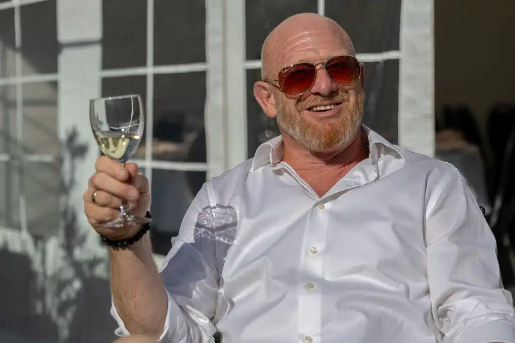 Skaldet mand med solbriller sidder med vinglas i hånden og nyder solen