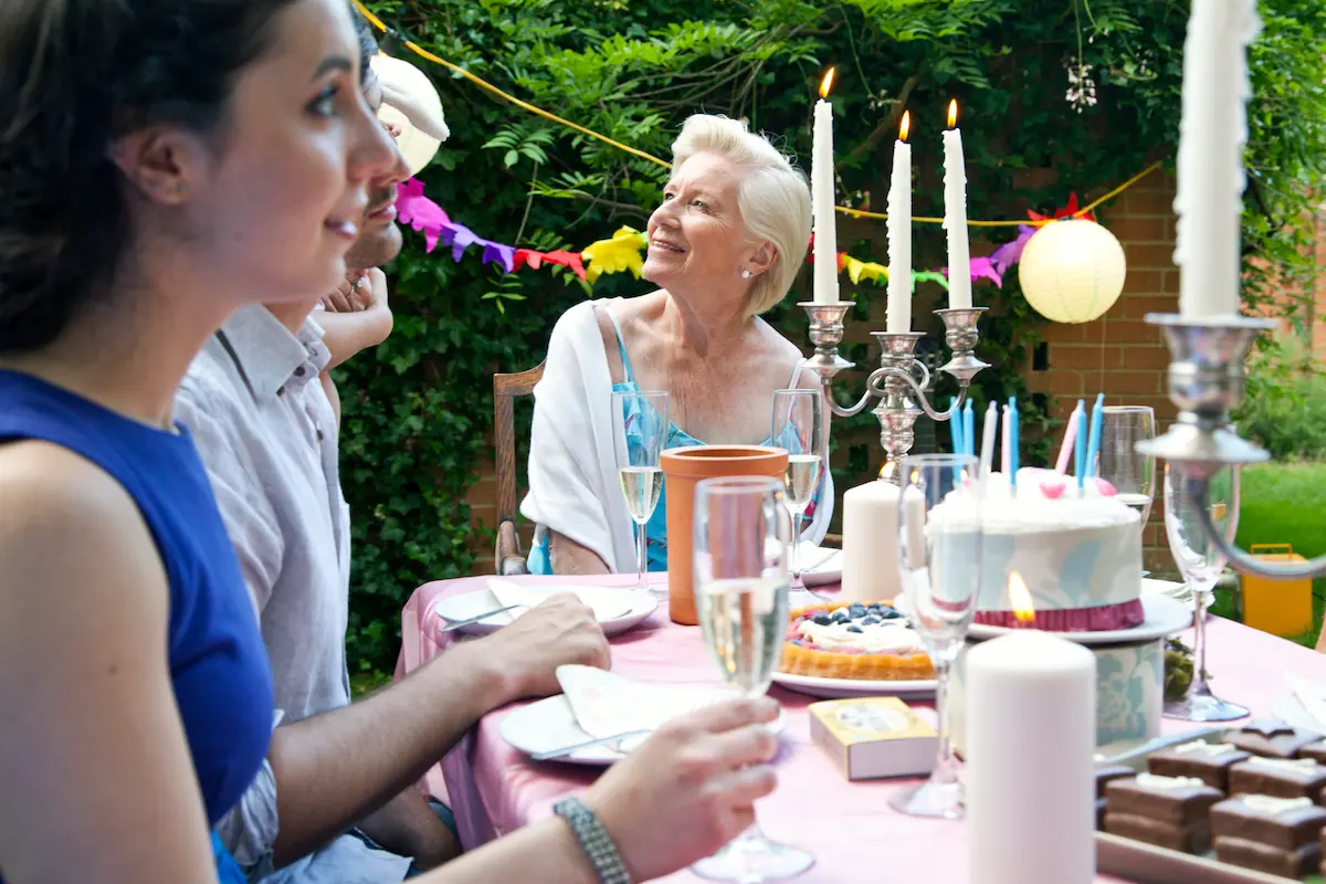 Festfotograferne har her fotograferet en fødselsdag, holdt i en have. På dette billede ses et dækket bord og man kan se 3 mennesker ved bordet. Det er sommer og personerne sidder i kortærmet tøj
