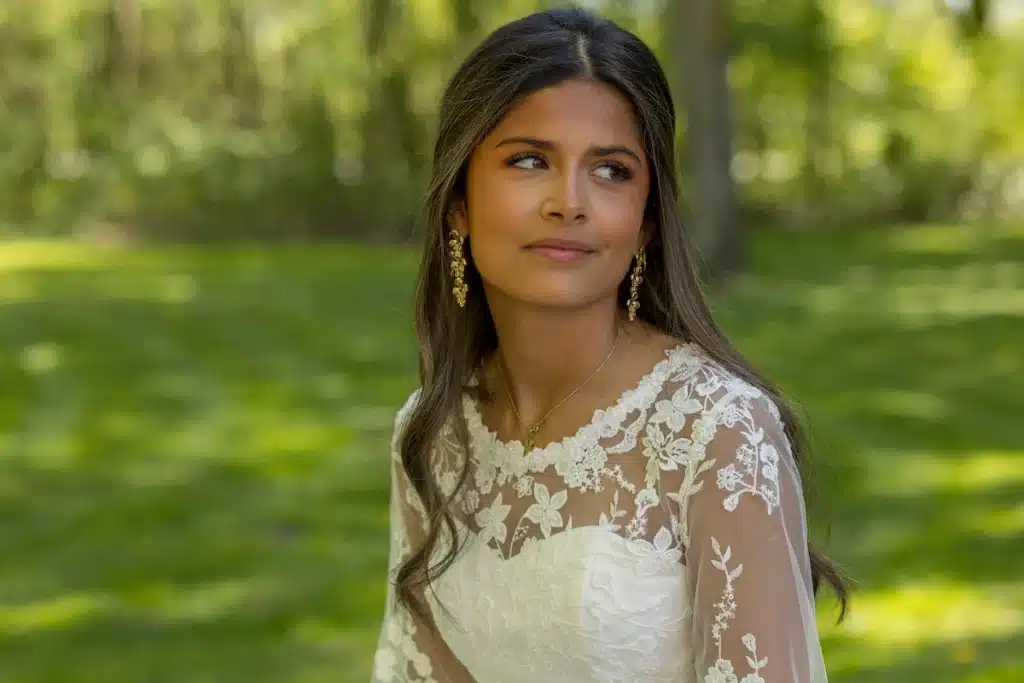 Konfirmationsfoto af pige i hvid blondekjole med blomstermønster og guldøreringe – professionelt konfirmationsfoto udendørs i grøn park