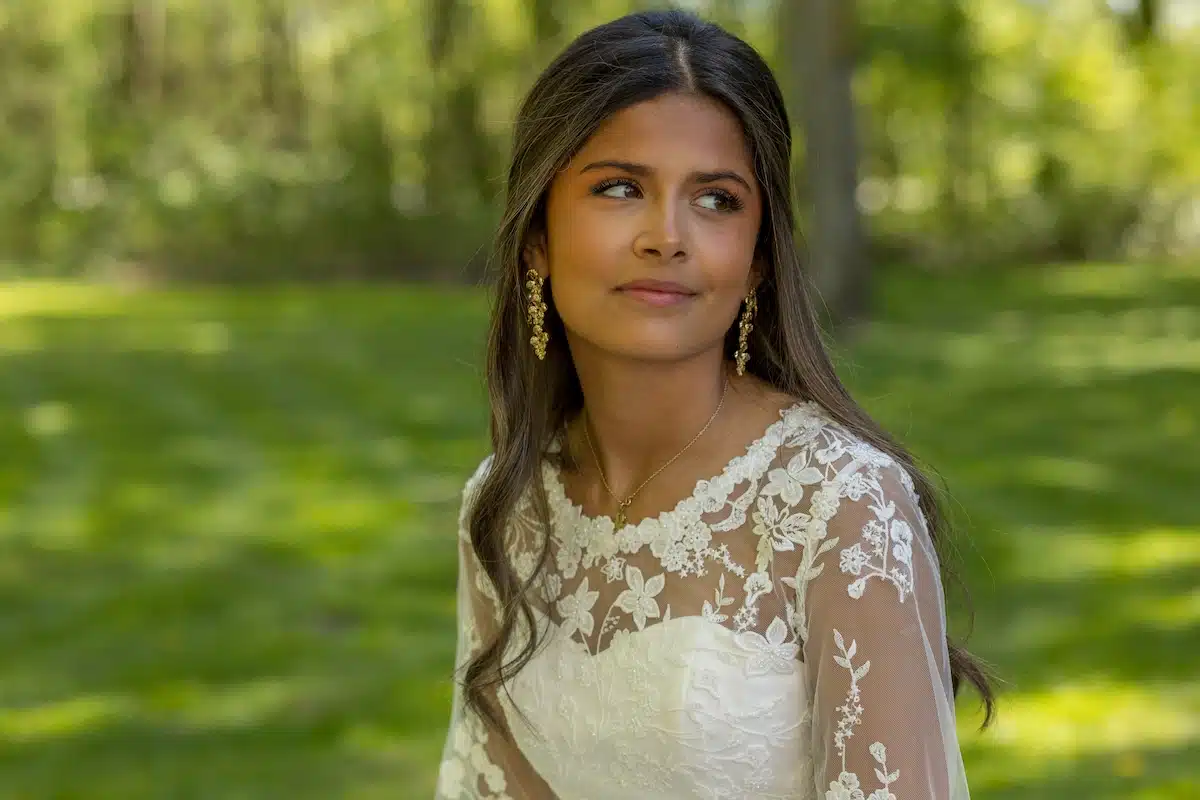 Konfirmationsfoto af pige i hvid blondekjole med blomstermønster og guldøreringe – professionelt konfirmationsfoto udendørs i grøn park