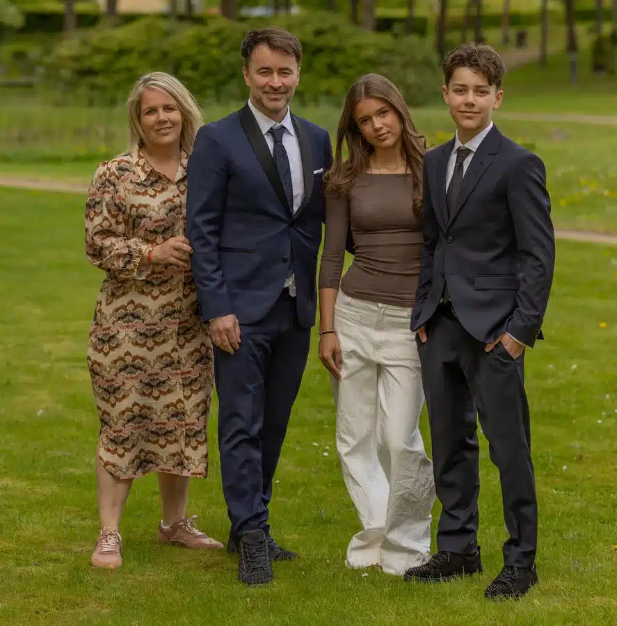 Familiefoto ved konfirmation – forældre og to teenagere fotograferet udendørs i grøn park – professionelt konfirmationsfoto