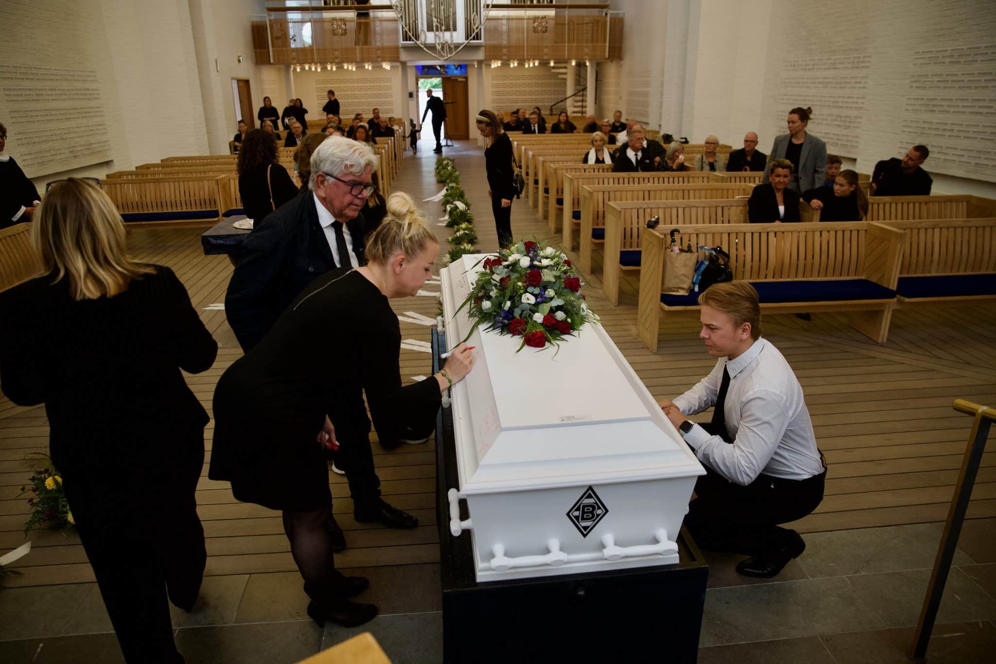 Fotografen har her fotograferet til en begravelse. På billedet ses kisten stå i kirken og flere af deltagerne er ved at skrive personlige beskeder på kisten