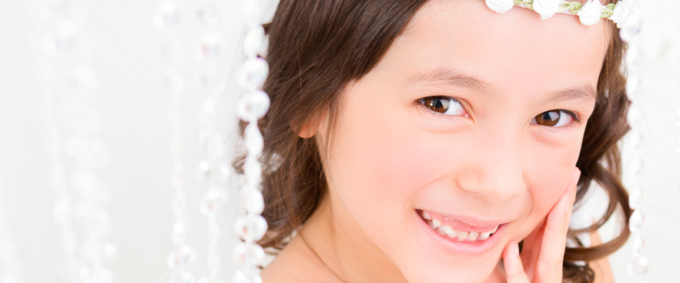 På billedet ses ansigtet af en smilende pige med langt mørkt hår og brune øjne.